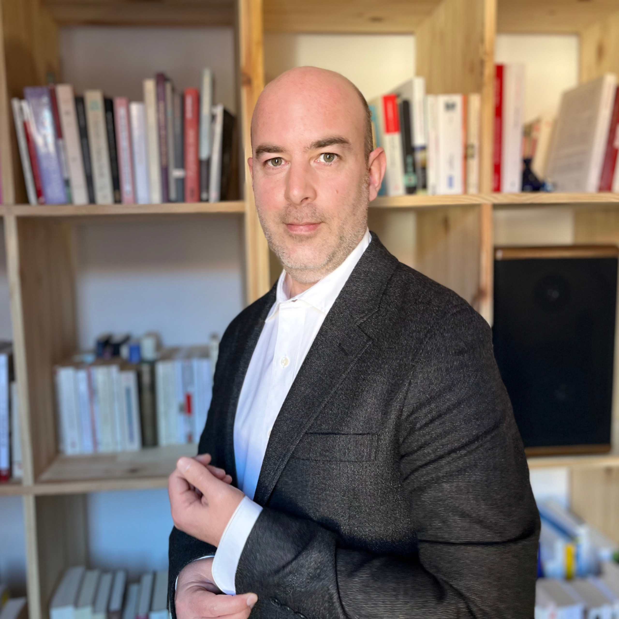 Portrait de Simon Icard, podcasteur, coordinateur éditorial et journaliste transmedia, posé devant une bibliothèque de livres.